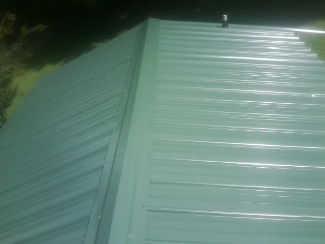 New green metal panels meeting at the ridge of a roof — Flat Roof Repair work by our crew in Denver