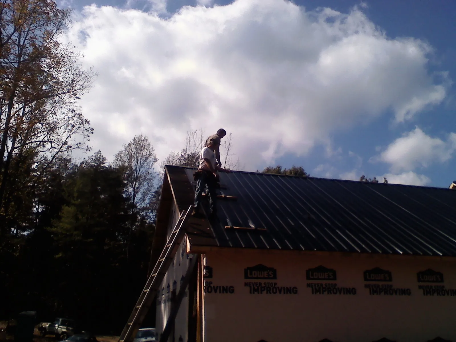 Roofer fastening dark metal panels high against a cloudy sky, from a Roof Inspection job in Denver